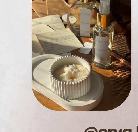 Vela em pote canelado branco com flor branca no topo, ao lado de difusor da marca Orva Home
